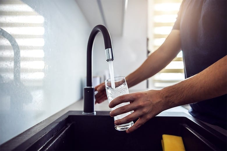 man-filling-glass-with-water-from-sink-faucet