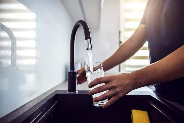 man-filling-glass-with-water-from-sink-faucet
